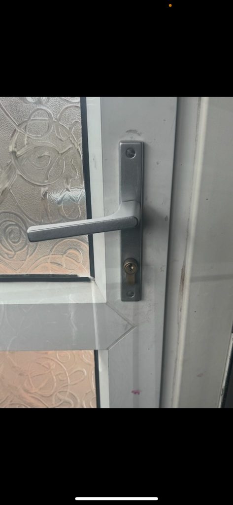 Silver door handle and lock on a white uPVC door with patterned glass